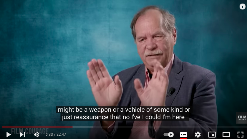 A speaker holding both palms open and forward, with the subtitle reading that something might be a weapon or a vehicle of some kind, or just reassurance.